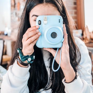 adolescent girl using a blue instant camera adolescent girl using a blue instant camera