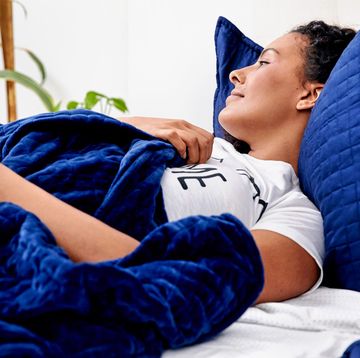 woman lying in bed with blue gravity blanket and pillows woman lying in bed with blue gravity blanket and pillows