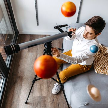 boy sitting on bed looking into telescope with planet mobile above his head boy sitting on bed looking into telescope with planet mobile above his head