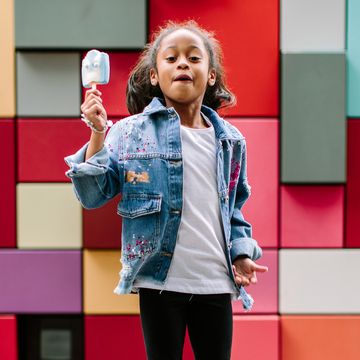 girl with popsicle jumping up against colorful tile background girl with popsicle jumping up against colorful tile background