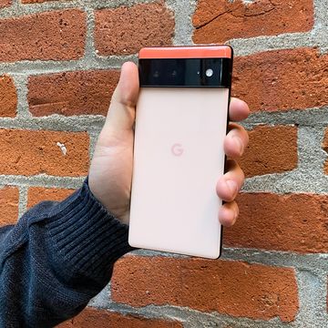 hand holding coral google pixel 6 in front of brick wall