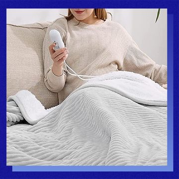 woman pressing buttons on heated blanket controller on couch
