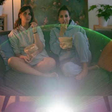 two women on couch in living room eating popcorn and watching a movie from a projector screen