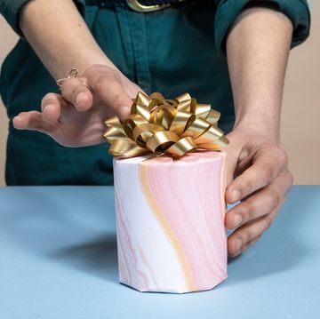 hands adjusting gold bow on gift wrapped candle