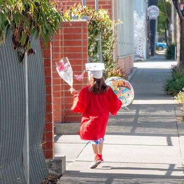 kid graduate carrying balloon and flowers