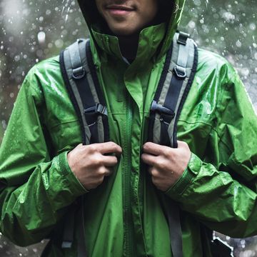 man standing in rain with backpack and green rain jacket