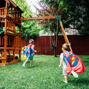 kids in superhero capes playing with wooden swing set
