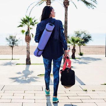 woman holding yoga mag and bag looking onto beach